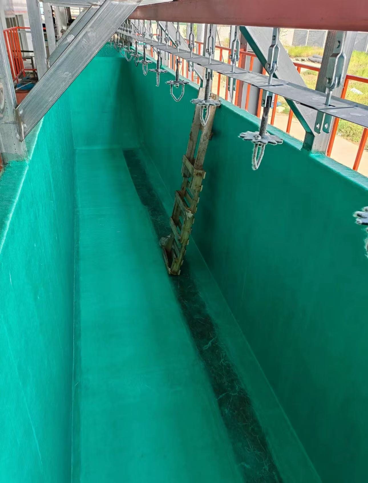 Von oben gesehenes GFK-ausgekleidetes E-Coating-Tauchbecken mit Hängeförderern und einer Zugangsleiter im Becken