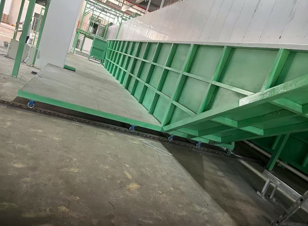 Grünes GFK-ausgekleidetes E-Coating-Becken mit externen Stahlversteifungen auf einer Bodentransferschiene neben der Beschichtungslinie