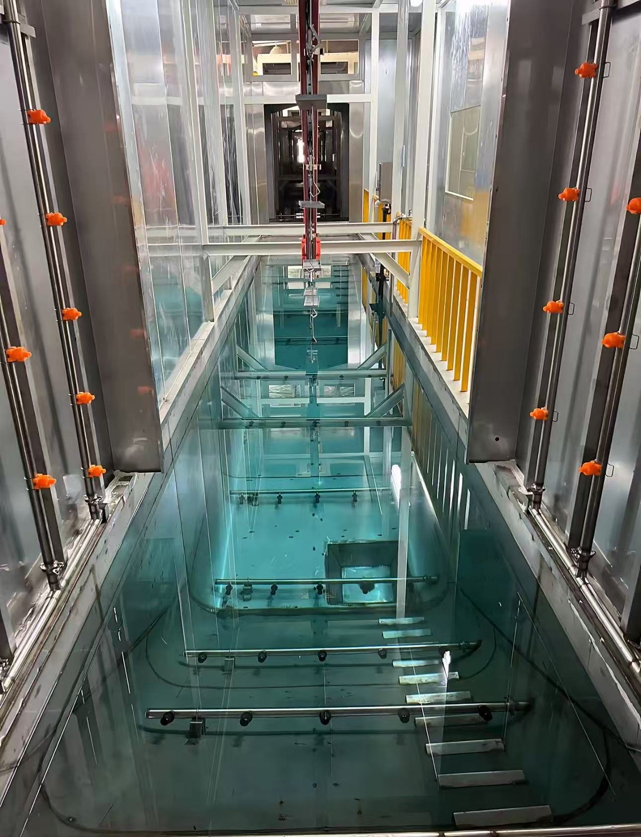 Gefüllter Spültank mit Sprühdüsen im geschlossenen Tunnel einer elektrophoretischen Beschichtungslinie, mit gelb umzäuntem Laufsteg