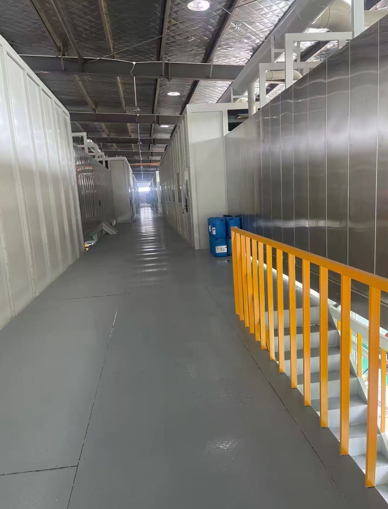 Wartungssteg mit gelbem Treppengeländer zwischen dem geschlossenen Vorbehandlungstunnel und der Beckenlinie einer E-Coating-Anlage