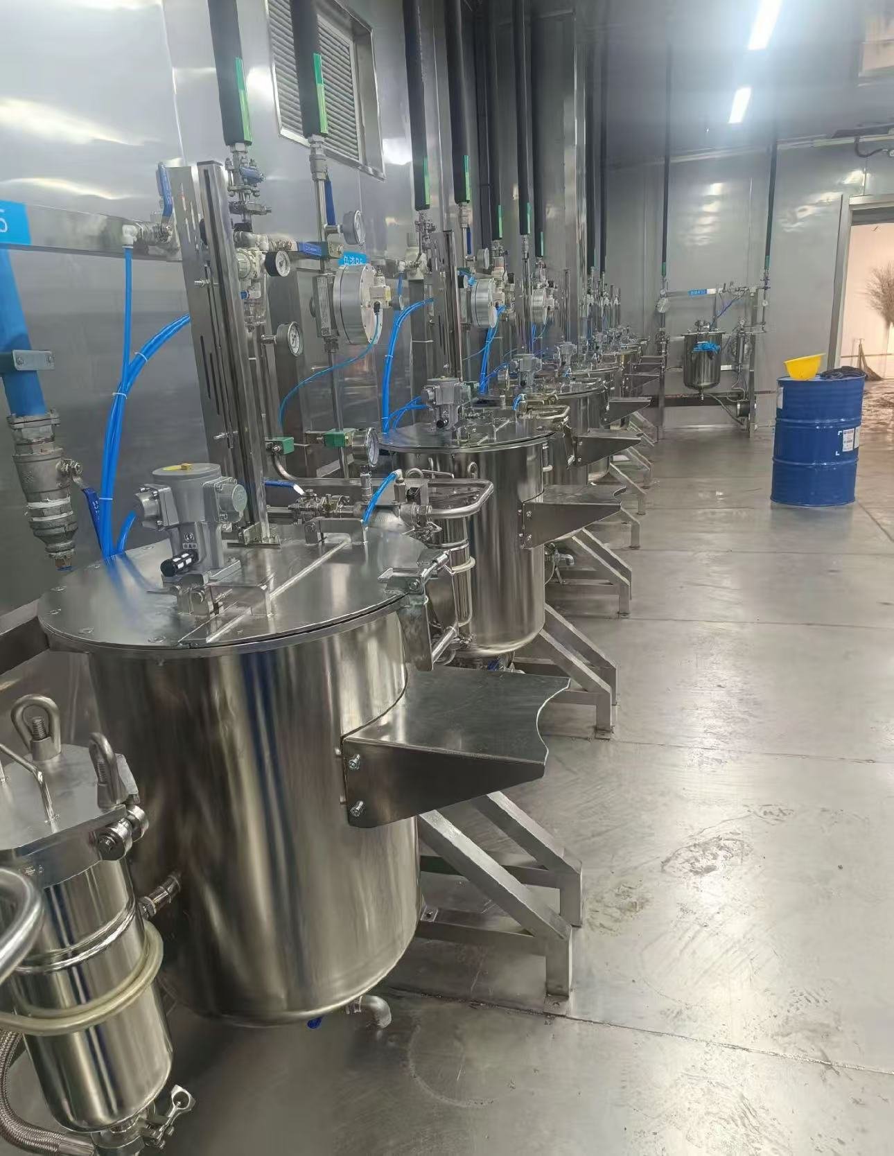 Stainless steel paint pressure tanks with pneumatic agitators and filter housings lined up in a paint mixing room