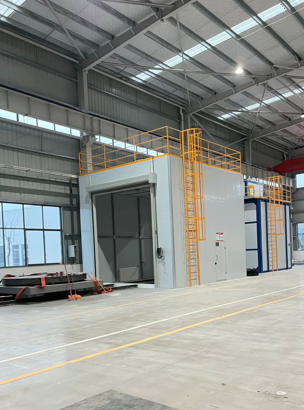Blue abrasive recovery elevator and cartridge dust collector with service platform beside a sandblasting room with exhaust ducts and control panel