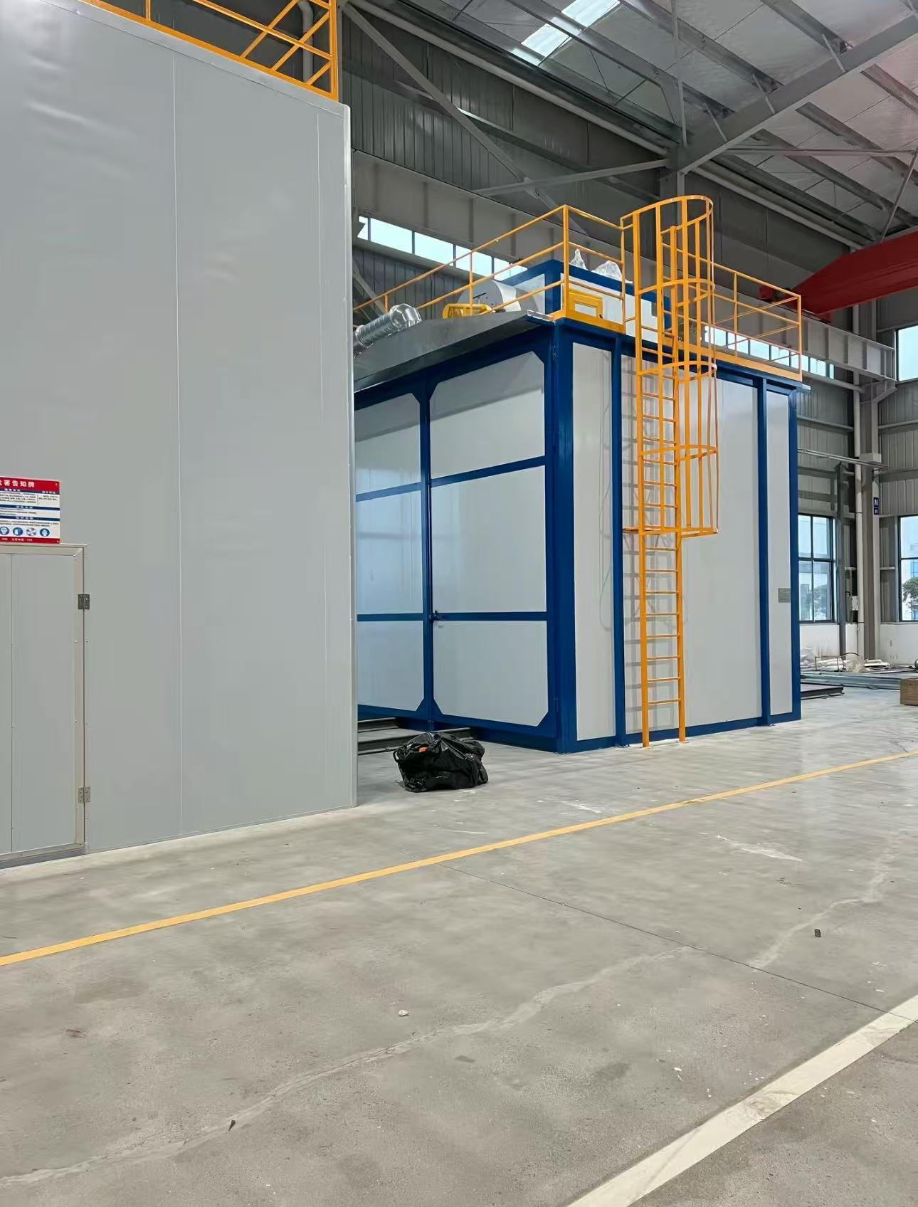 Blue-framed enclosure of a sandblasting room with yellow roof railing and caged access ladder next to the blow-off room wall