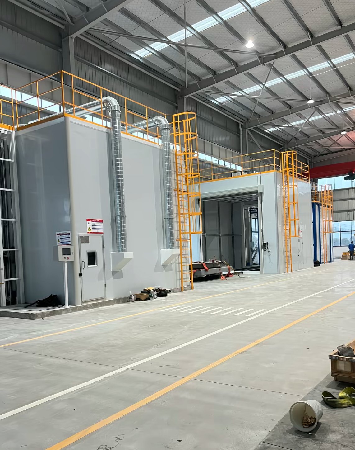 Row of enclosed blasting and painting rooms with yellow roof platforms, access ladders and a blue-framed room at the end