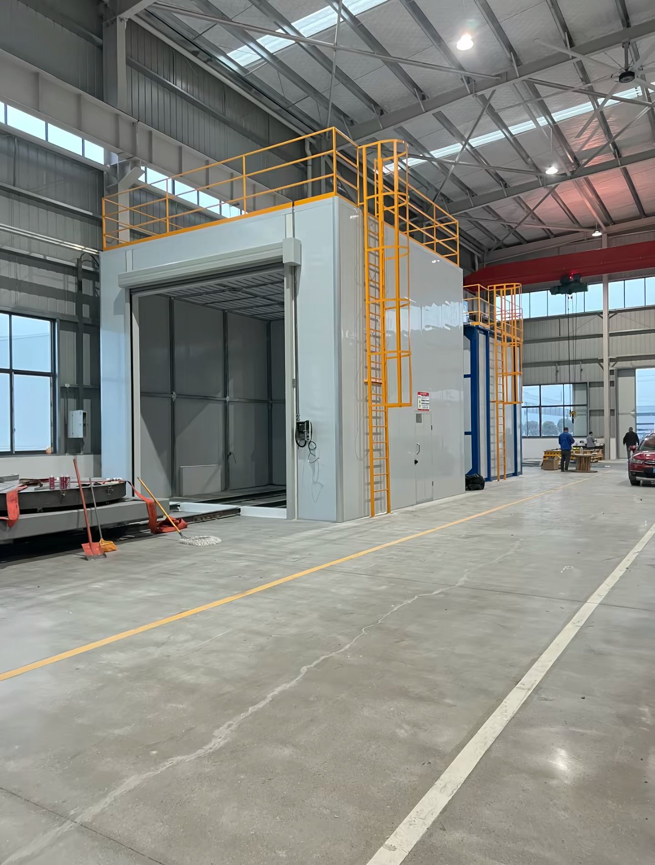 Enclosed blasting room with roll-up door open, grated floor, roof platform and yellow access ladder