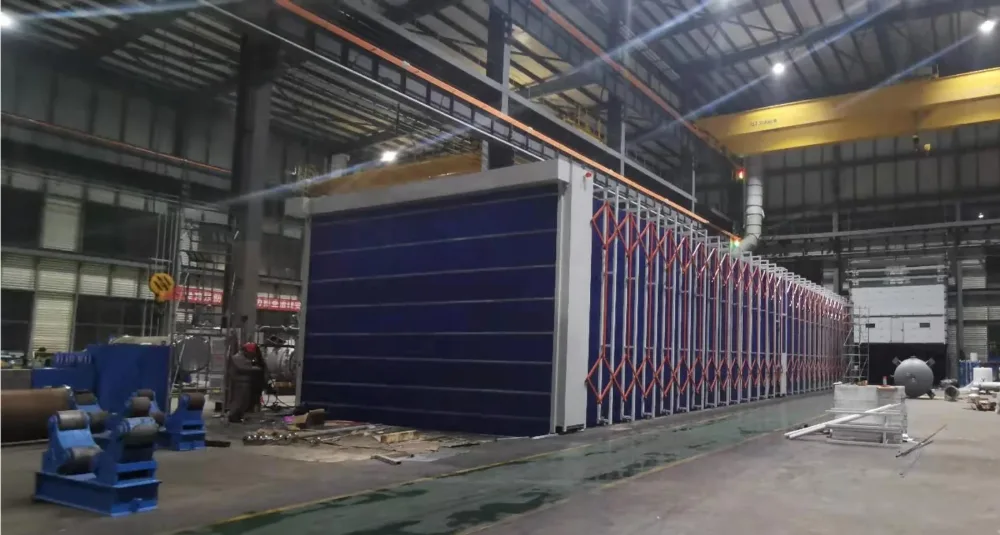 Longue cabine de pulvérisation télescopique avec tissu PVC ignifuge bleu et cadres pliants orange dans un hall de fabrication lourde avec ponts roulants