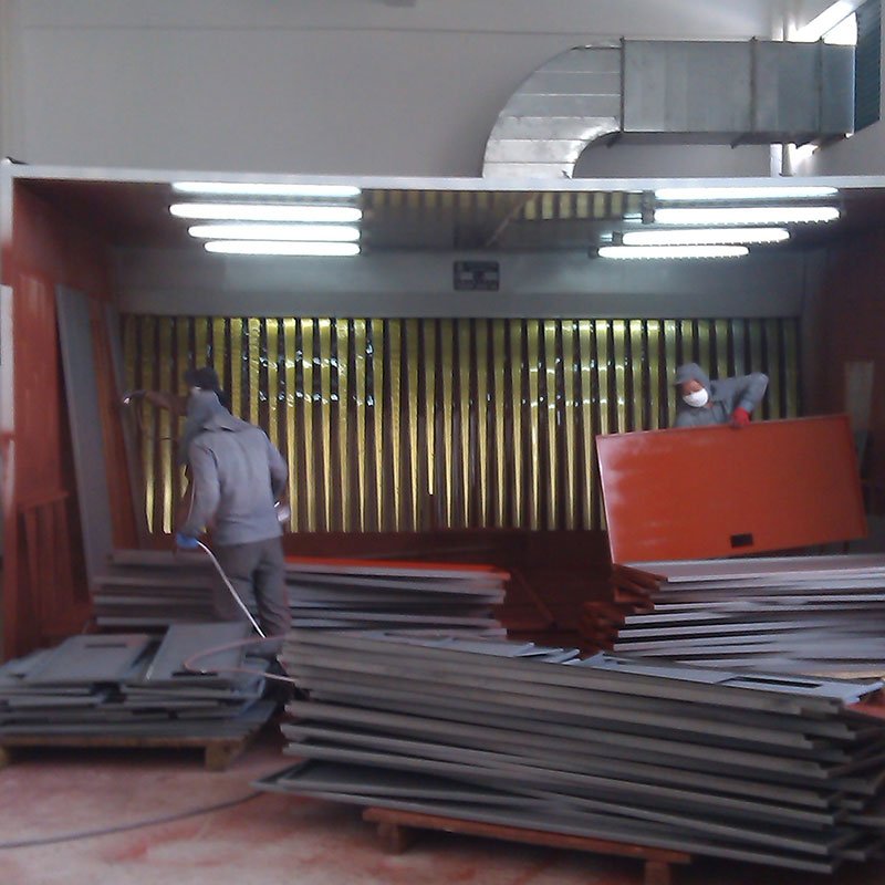 Operators spray-painting steel panels in front of a corrugated dry filter wall inside a spray booth